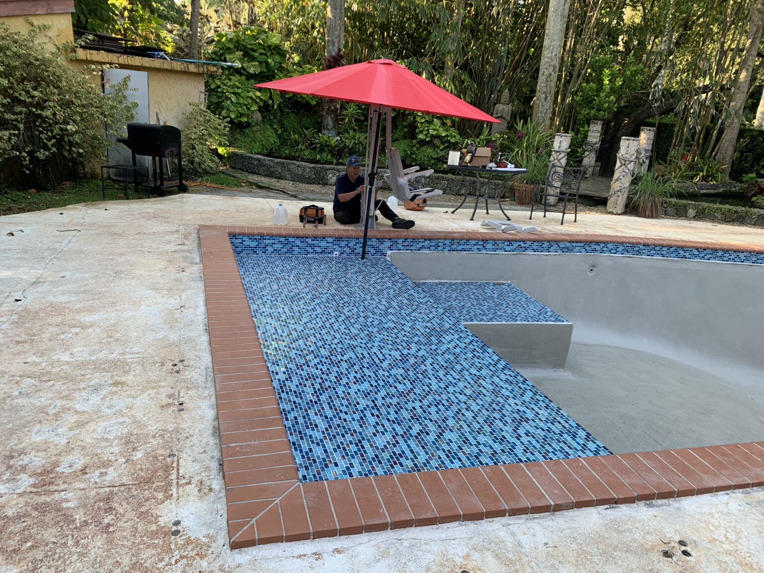 Swimming pool renovation with blue mosaic tile installation in progress