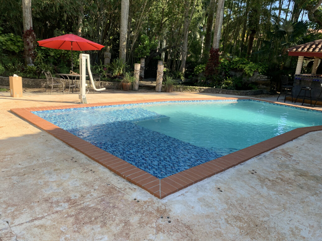 Renovated backyard swimming pool with blue mosaic tile and brick coping