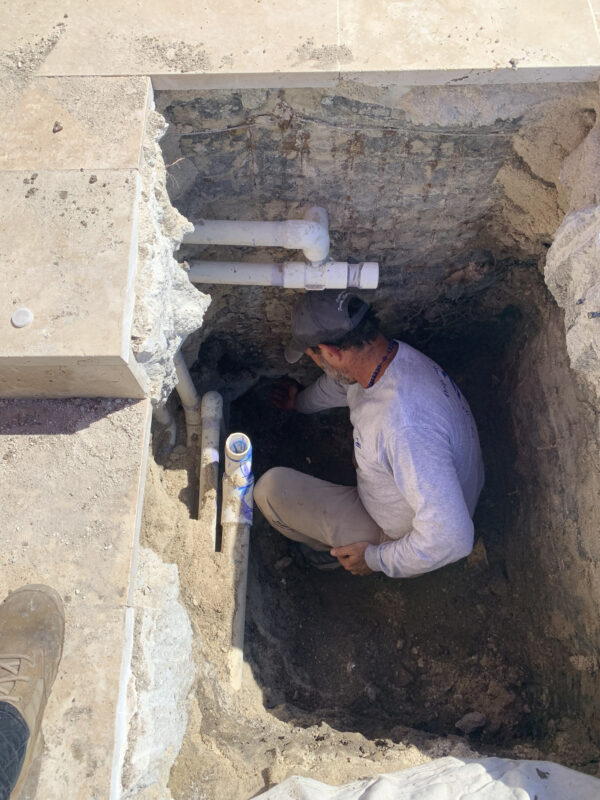 Pool technician inspecting exposed plumbing near a spa main drain