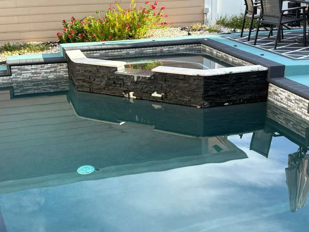 Backyard pool with stone spa and tile trim.