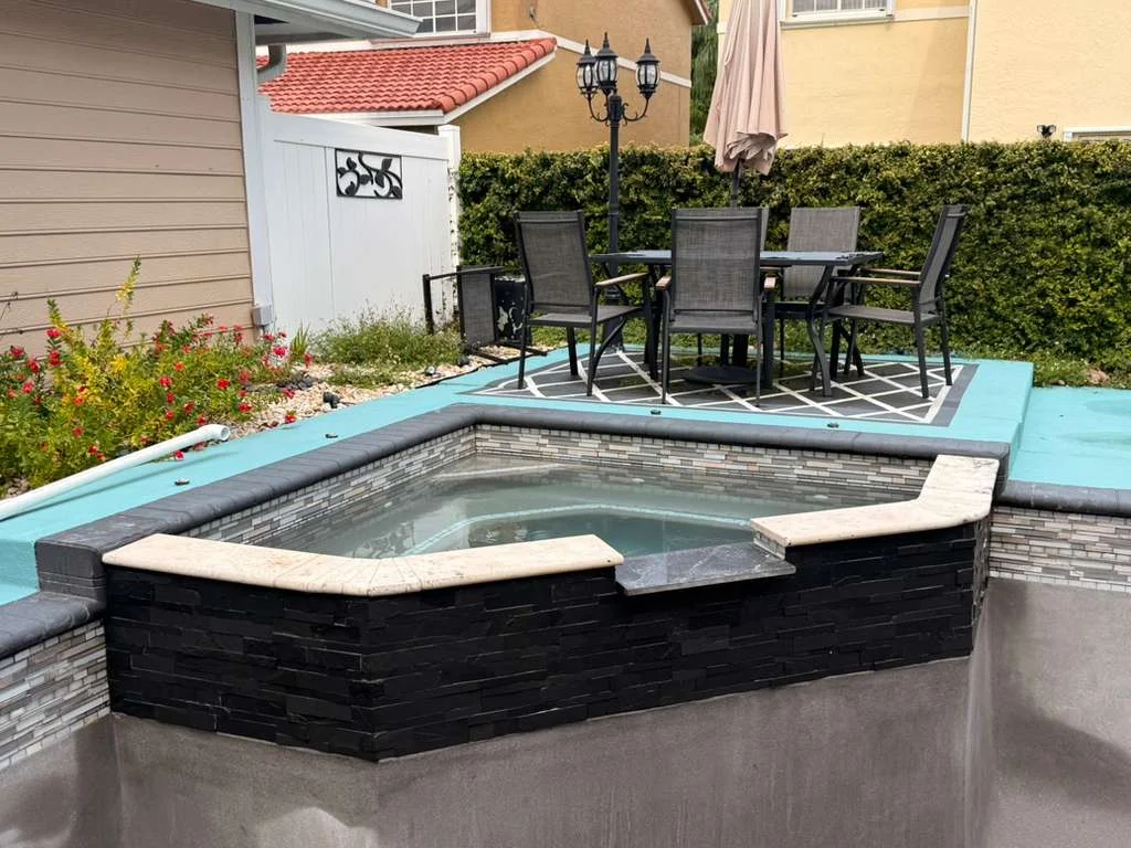 Backyard pool and spa with dark stone wall and patio dining area.